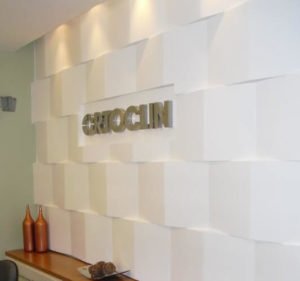Painel da recepção em 3D feito com gesso acartonado criado por Carol Cunha Design. Foquinhos de led para dar efeito de profundidade com jogo de sombras e nome da clínica em letras de inox.